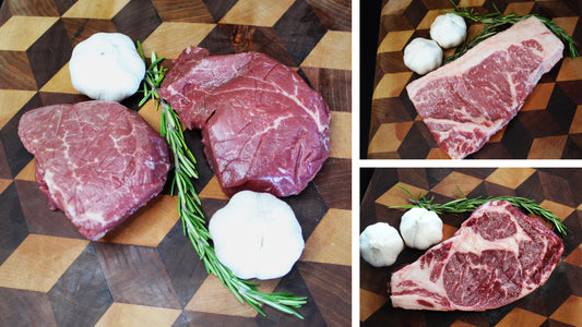 Two pieces of raw steak with garlic bulbs and rosemary on a wooden cutting board.