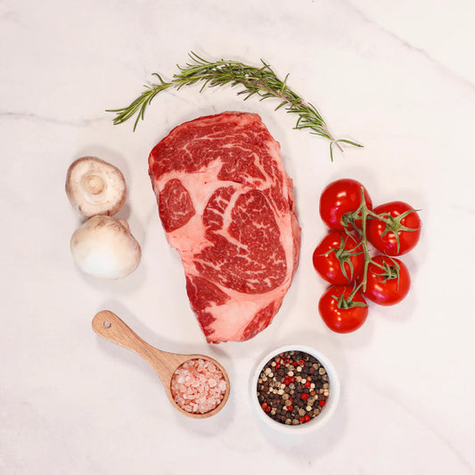 Raw Ribeye steak with vegetables and spices on a white background